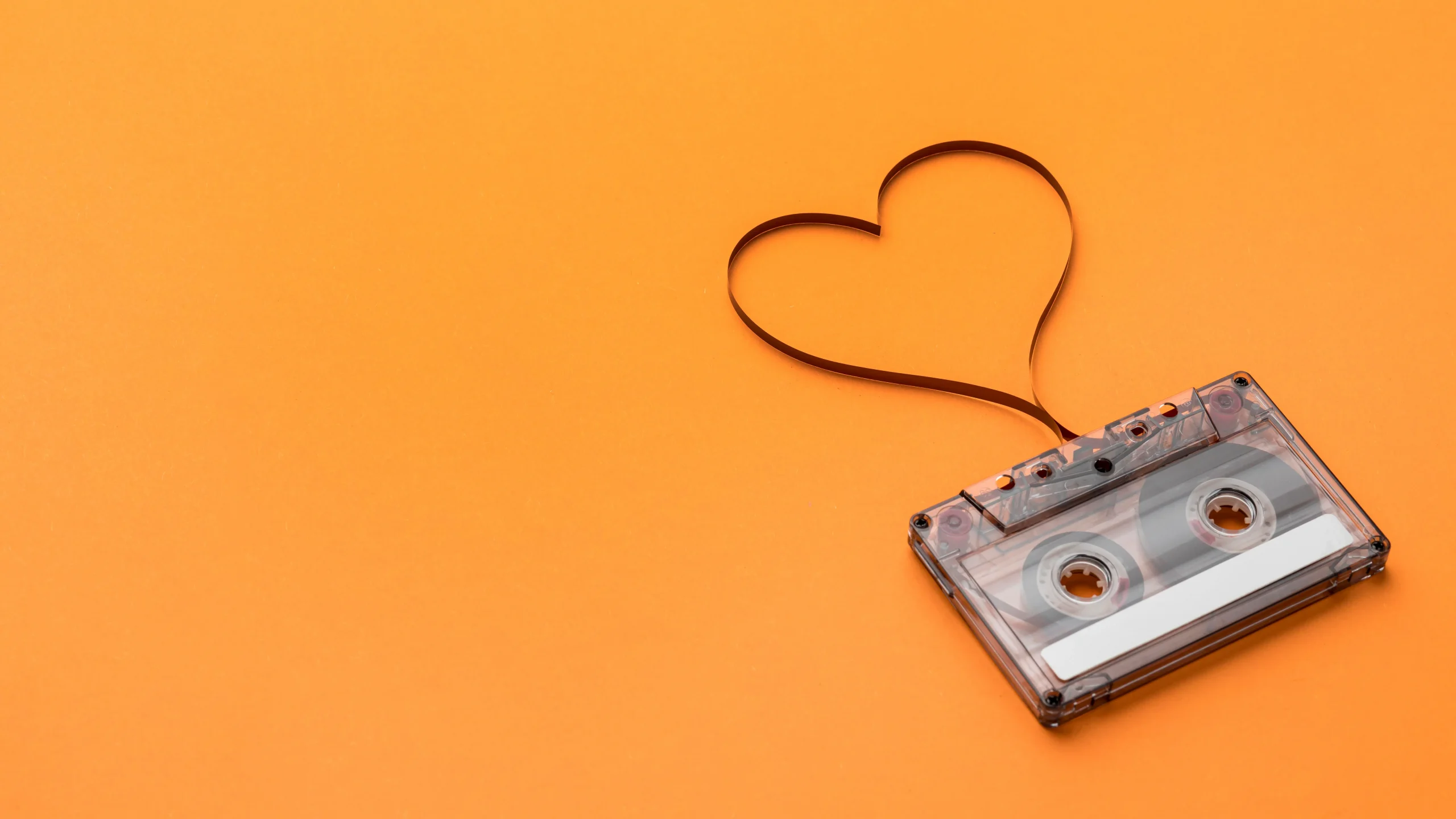 A cassette tape with recording film in the shape of a heart on an orange background